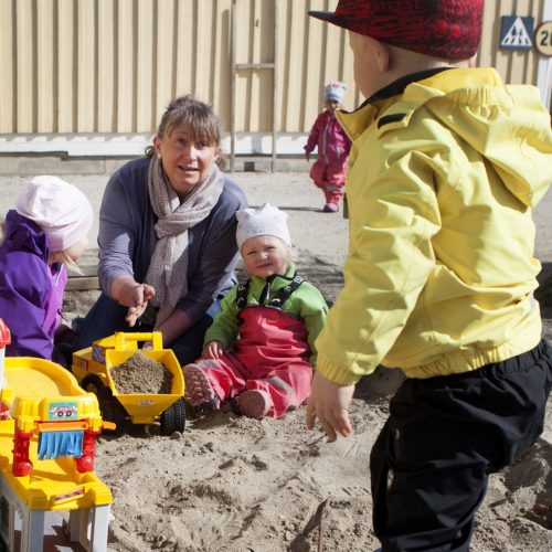 Förskolelärare med fyra barn i en sandlåda.